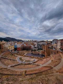 Stunning view of an ancient Roman amphitheater nestled amidst a modern cityscape under a dramatic sky.