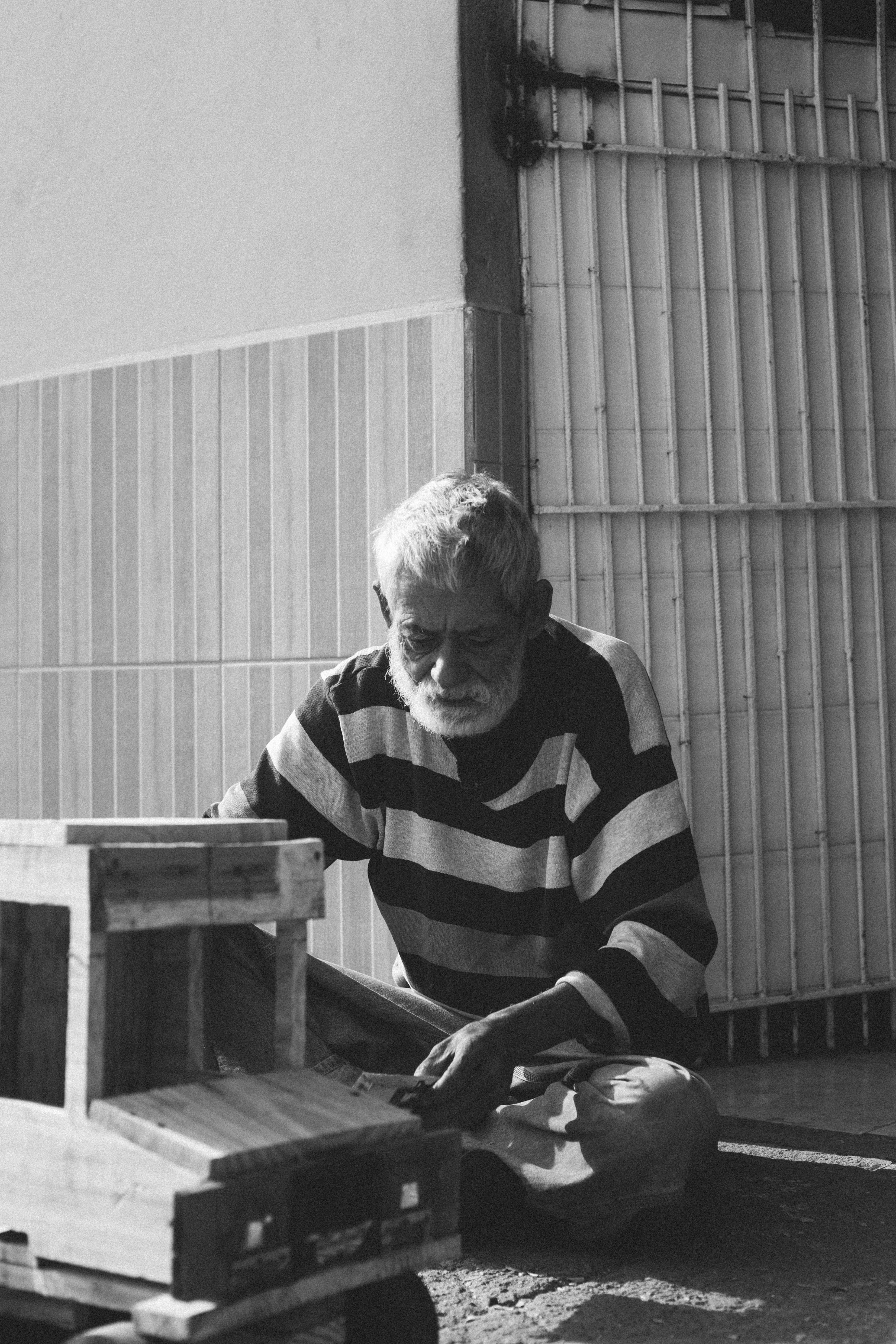 Black and white photo of a senior man crafting wooden toys outside a garage.