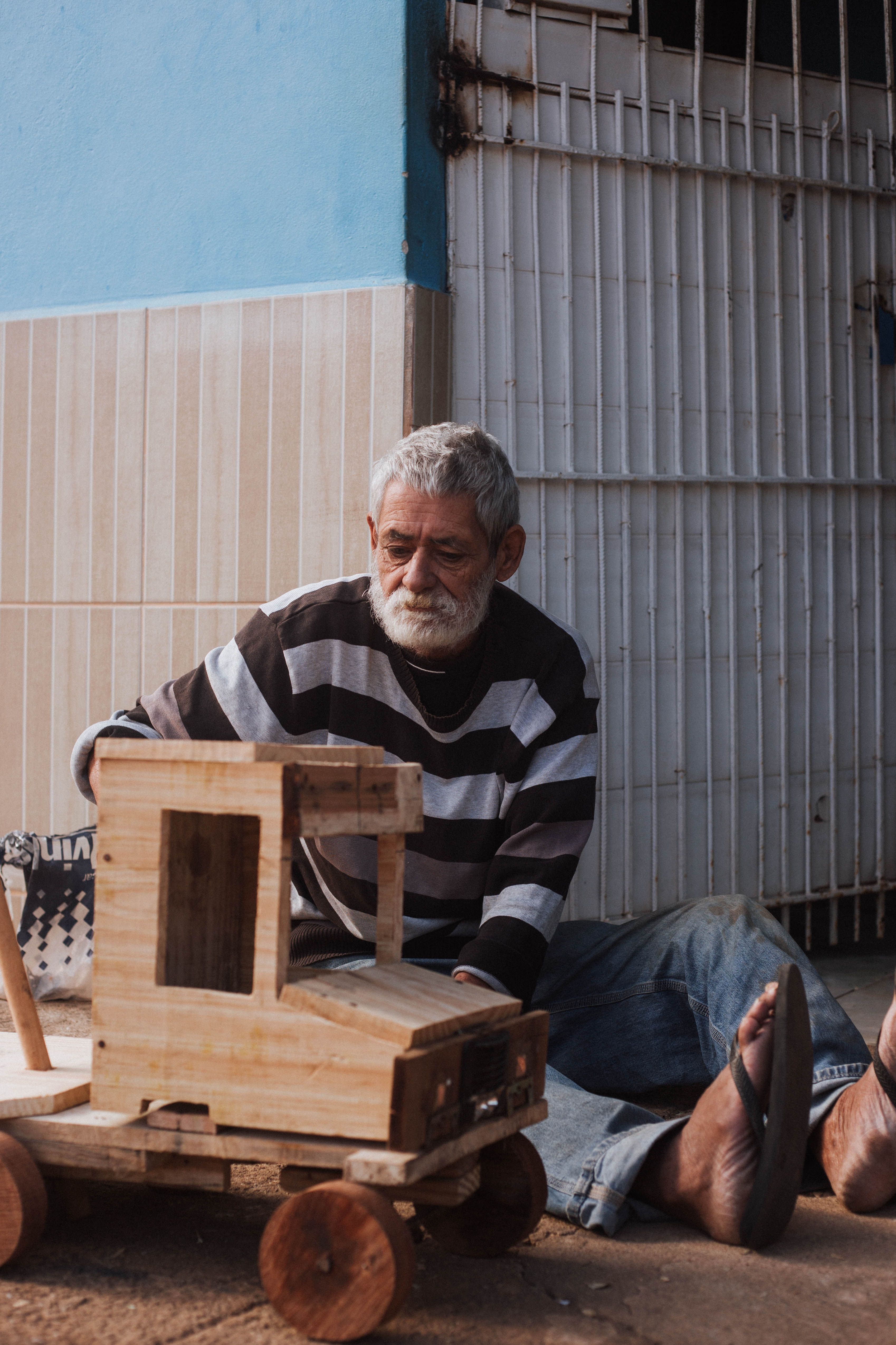 An elderly man skillfully crafts a wooden toy vehicle outdoors in Tarumirim, Brazil.