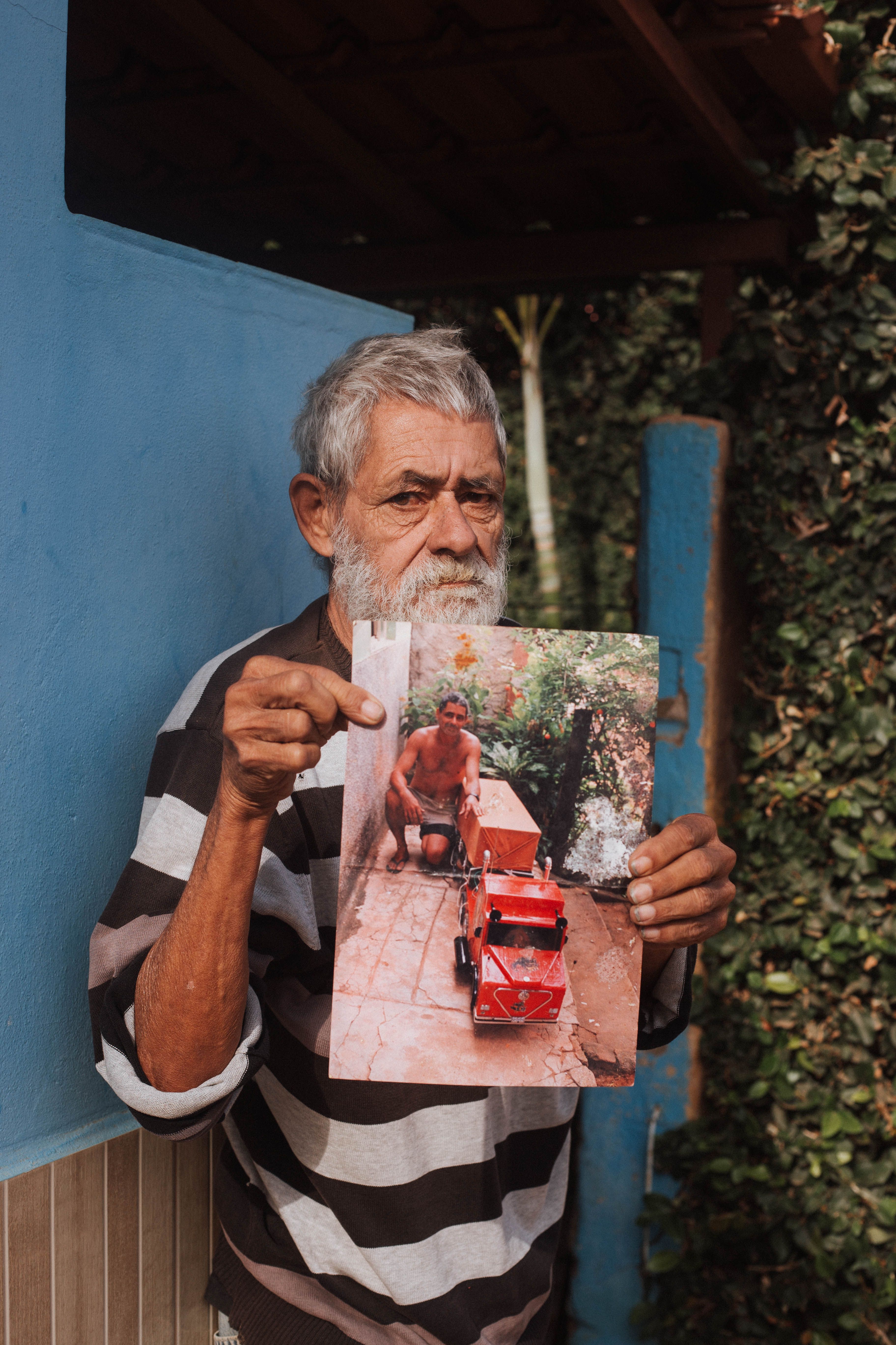 Elderly man displaying an old photograph outdoors in Tarumirim, Brazil.