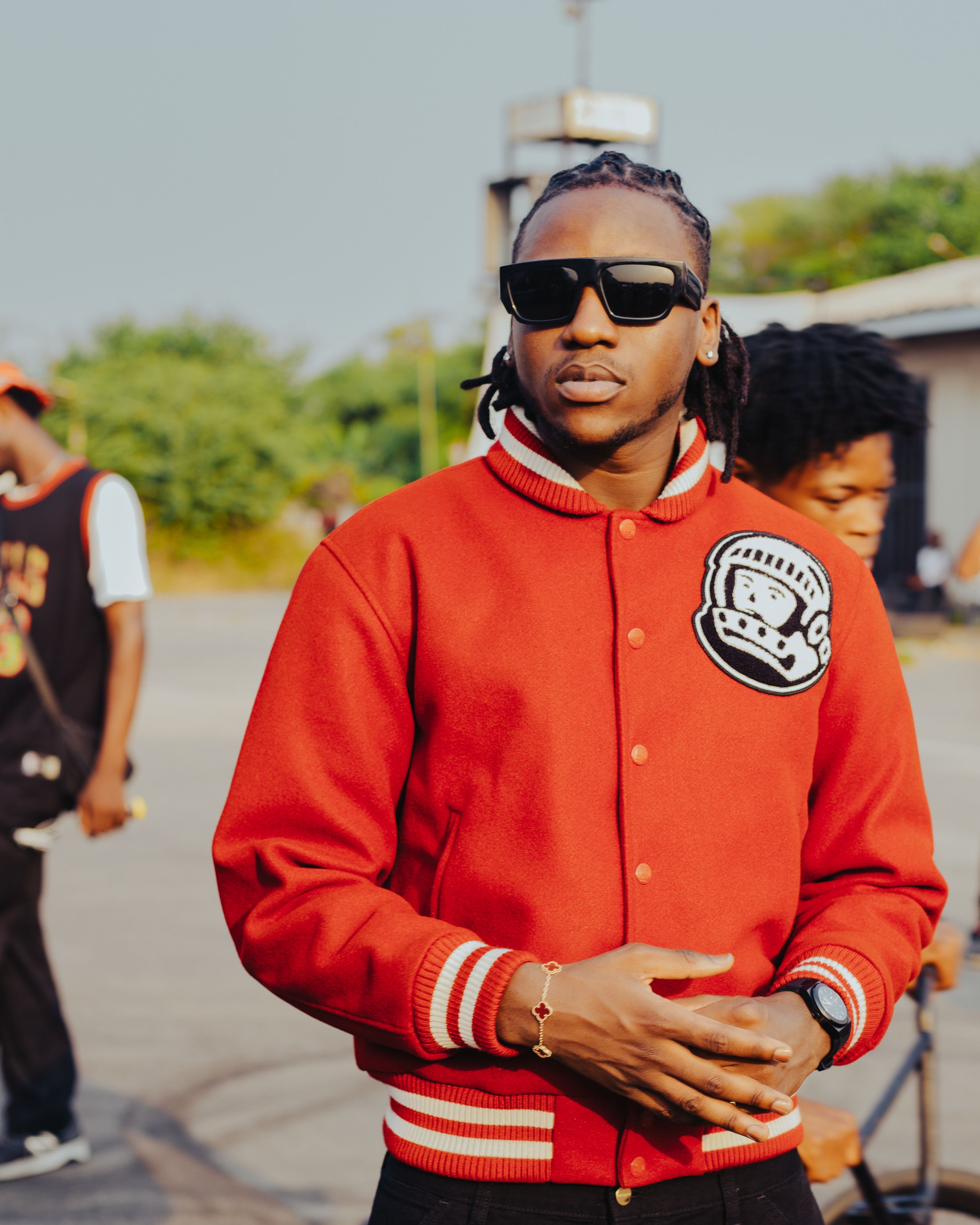 Young man in sunglasses and red jacket standing outdoors with friends.