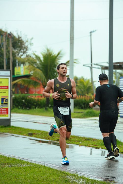 Free Two athletes running in a marathon during rainy weather, surrounded by lush greenery. Stock Photo