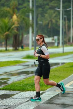 Woman in athletic gear running on a wet path in a tropical setting.
