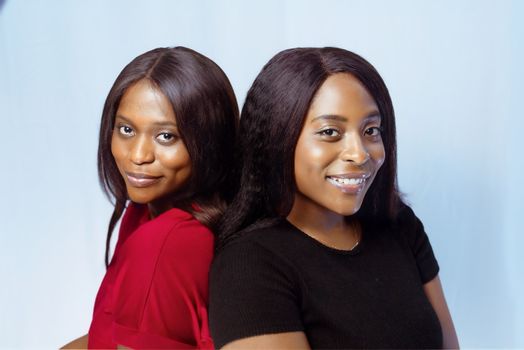 Two women standing back to back, smiling, with a light blue background.