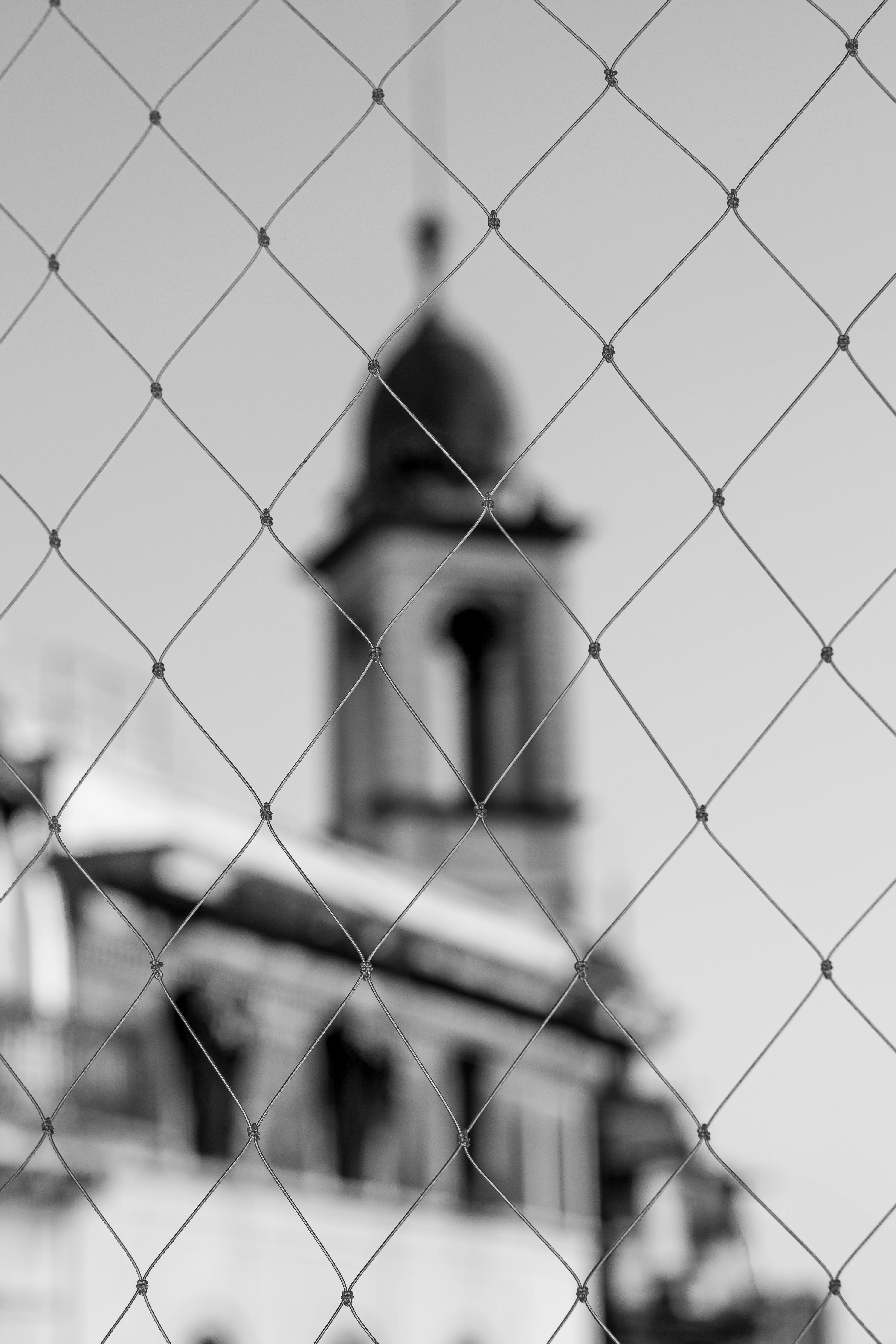 бесплатная Монохромное изображение церковной башни Буэнос-Айреса, вид через забор, подчеркивающее городскую архитектуру. Стоковое фото