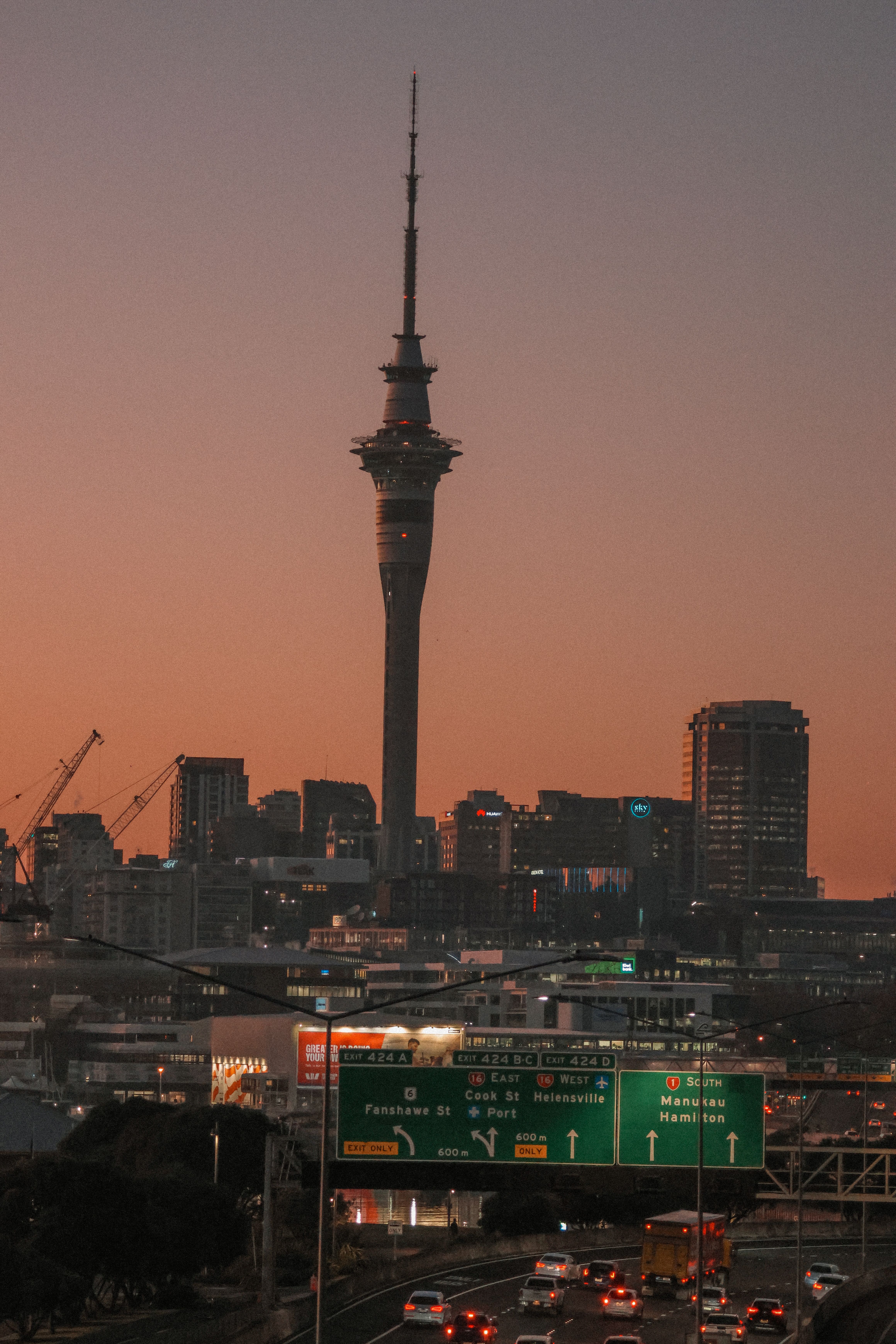 Scenic view of Auckland skyline featuring the Sky Tower at sunrise with city traffic below.