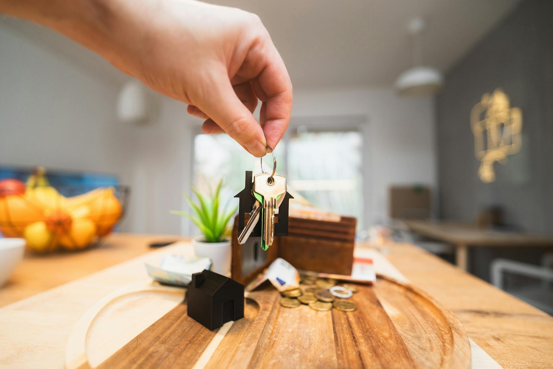 Hand holding keys in a modern living room setting, symbolizing home ownership or real estate investment.