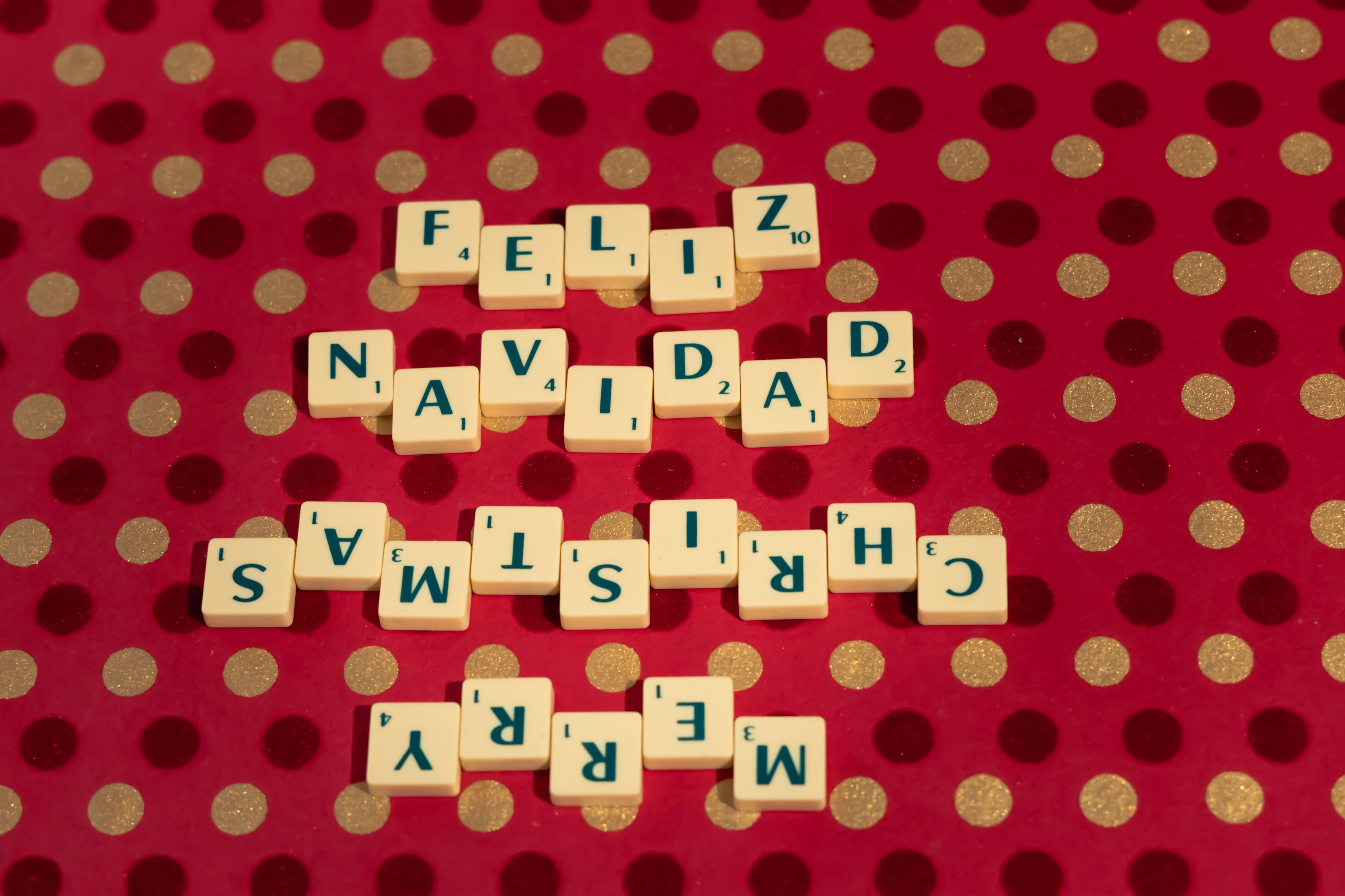 Scrabble tiles spelling 'Feliz Navidad Merry Christmas' on a festive polka dot backdrop.