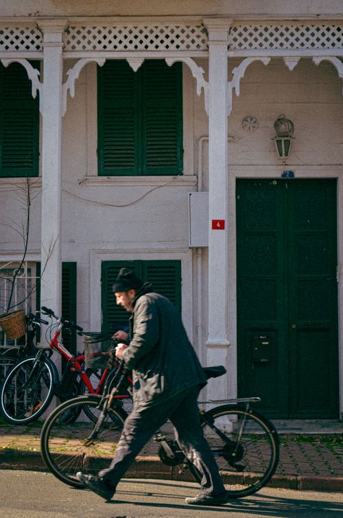 Free An elderly man walks a bicycle past a historic building on a sunny day. Stock Photo
