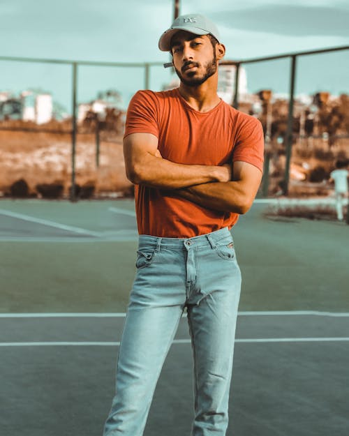 Man Wearing Orange Crew-neck T-shirt and Blue Denim Jeans Standing on a Court