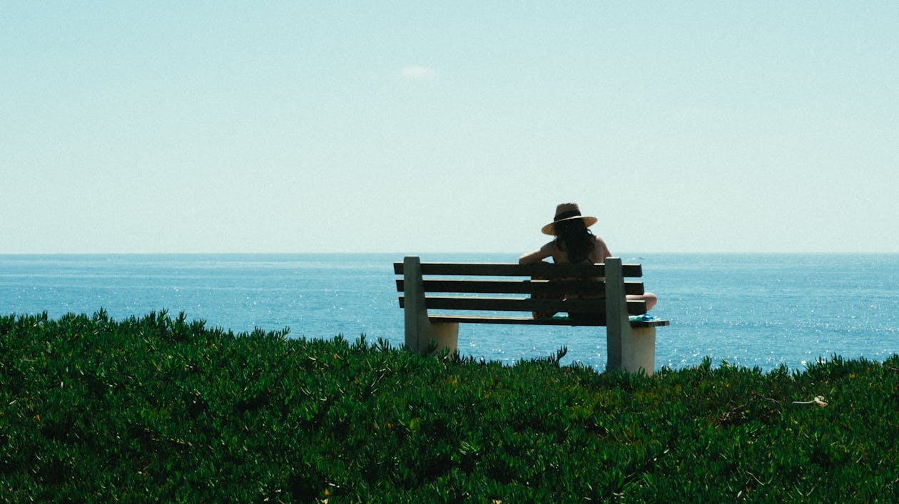 Free Woman Sitting on Bench on Grass Shore during Day Stock Photo