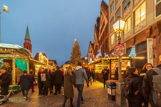 Festive Christmas market in a European city, bustling with people and lights.