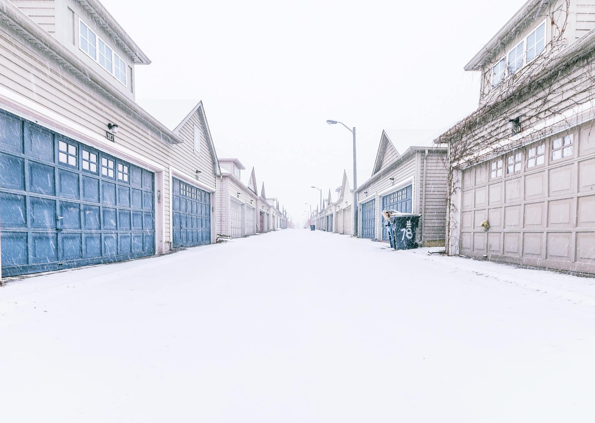 Snowy alley lined with residential garages in winter, creating a serene and cold atmosphere.