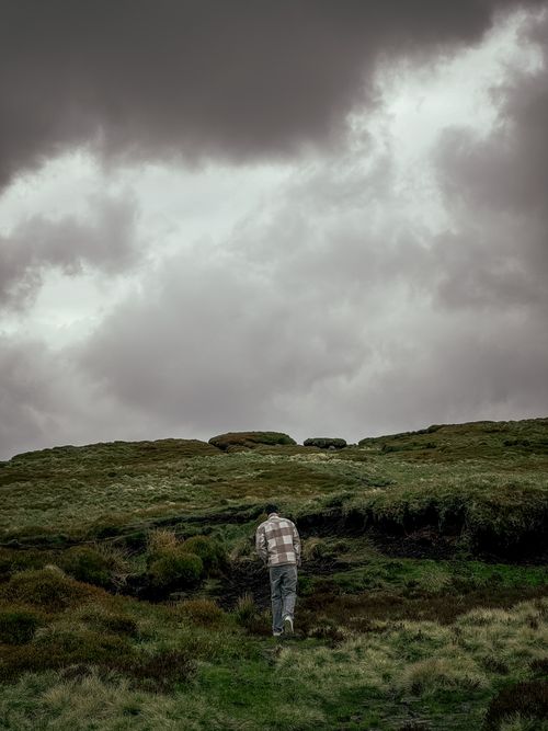 Free A lone individual walking up a lush grassy hill under a moody, overcast sky. Stock Photo