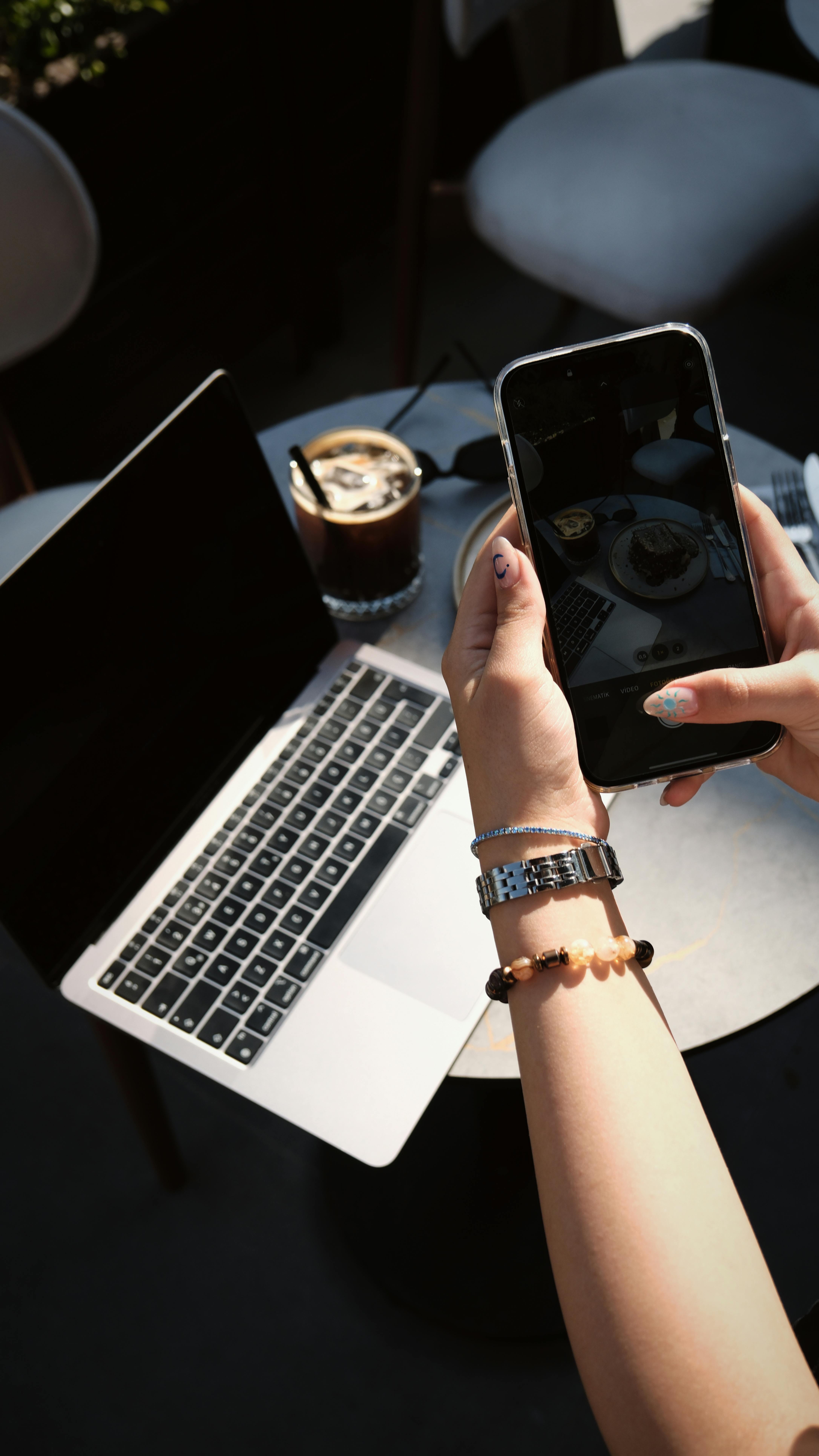 Hand holding smartphone capturing cafe scene with laptop and coffee.