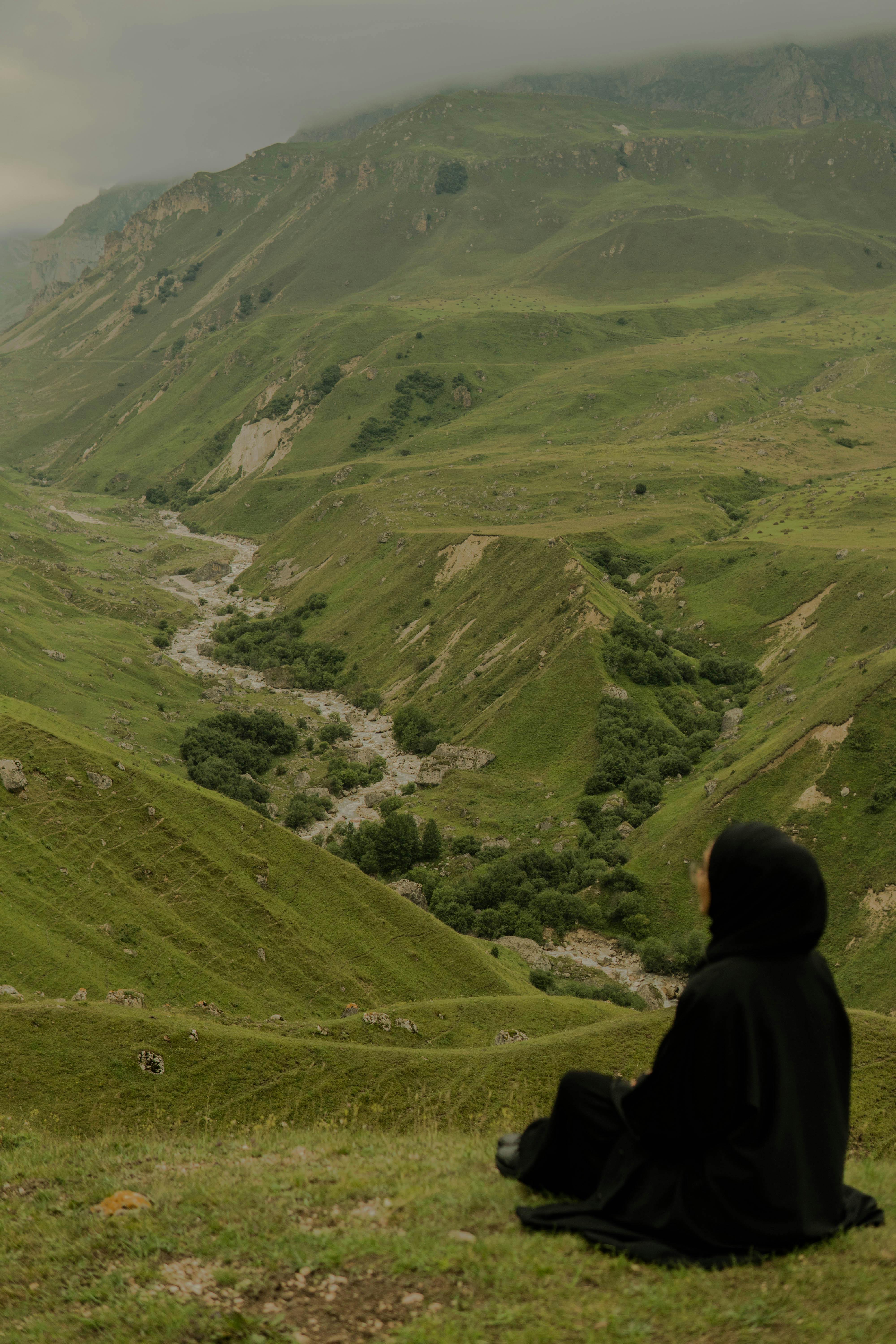 Person in black sitting calmly overlooking lush green valleys in Azerbaijani mountains.