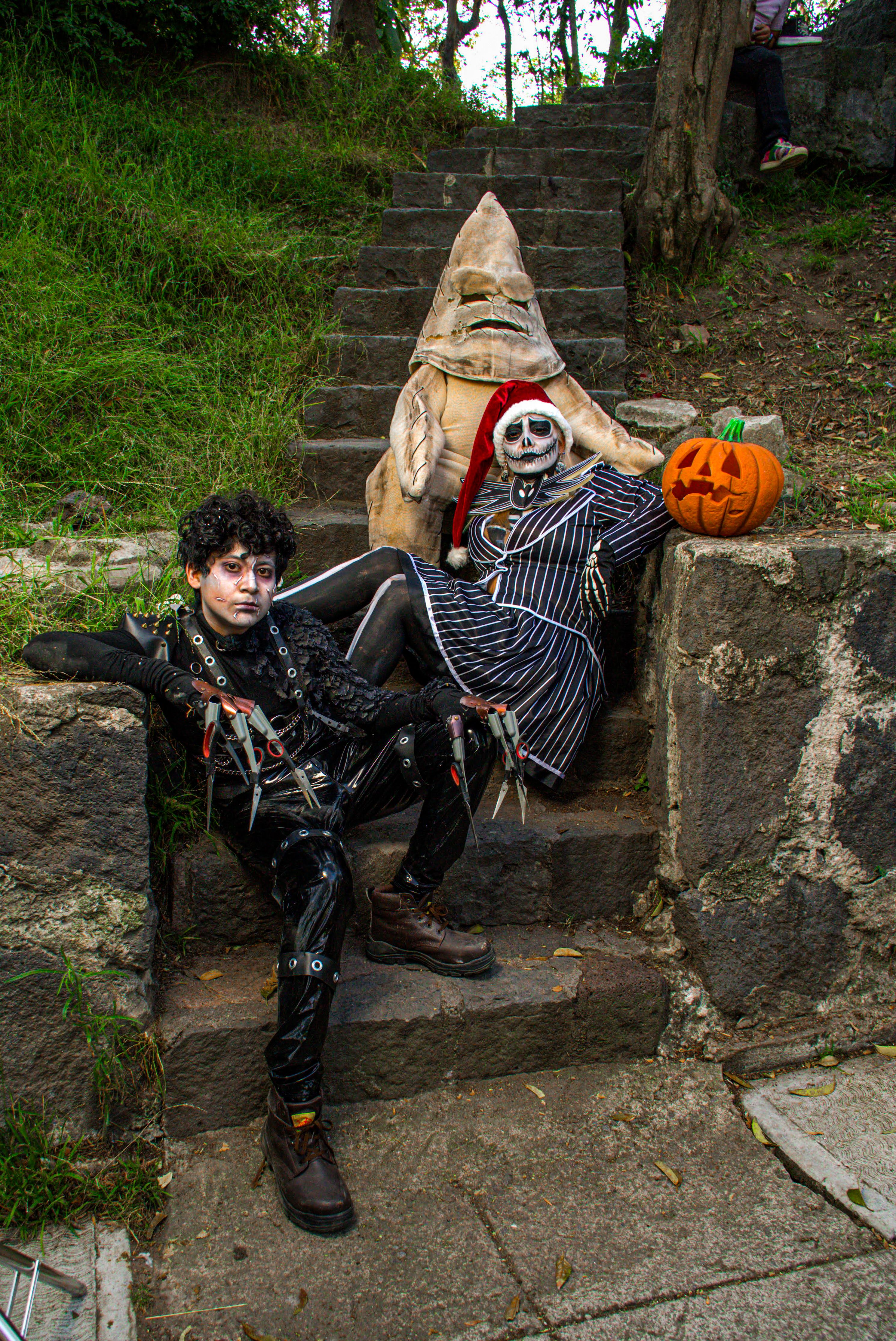 Drei Personen in kreativen Halloween-Kostümen posieren auf Außentreppen mit einem Kürbis.