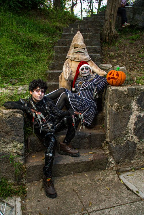 Free Three people in creative Halloween costumes posing on outdoor steps with a pumpkin. Stock Photo