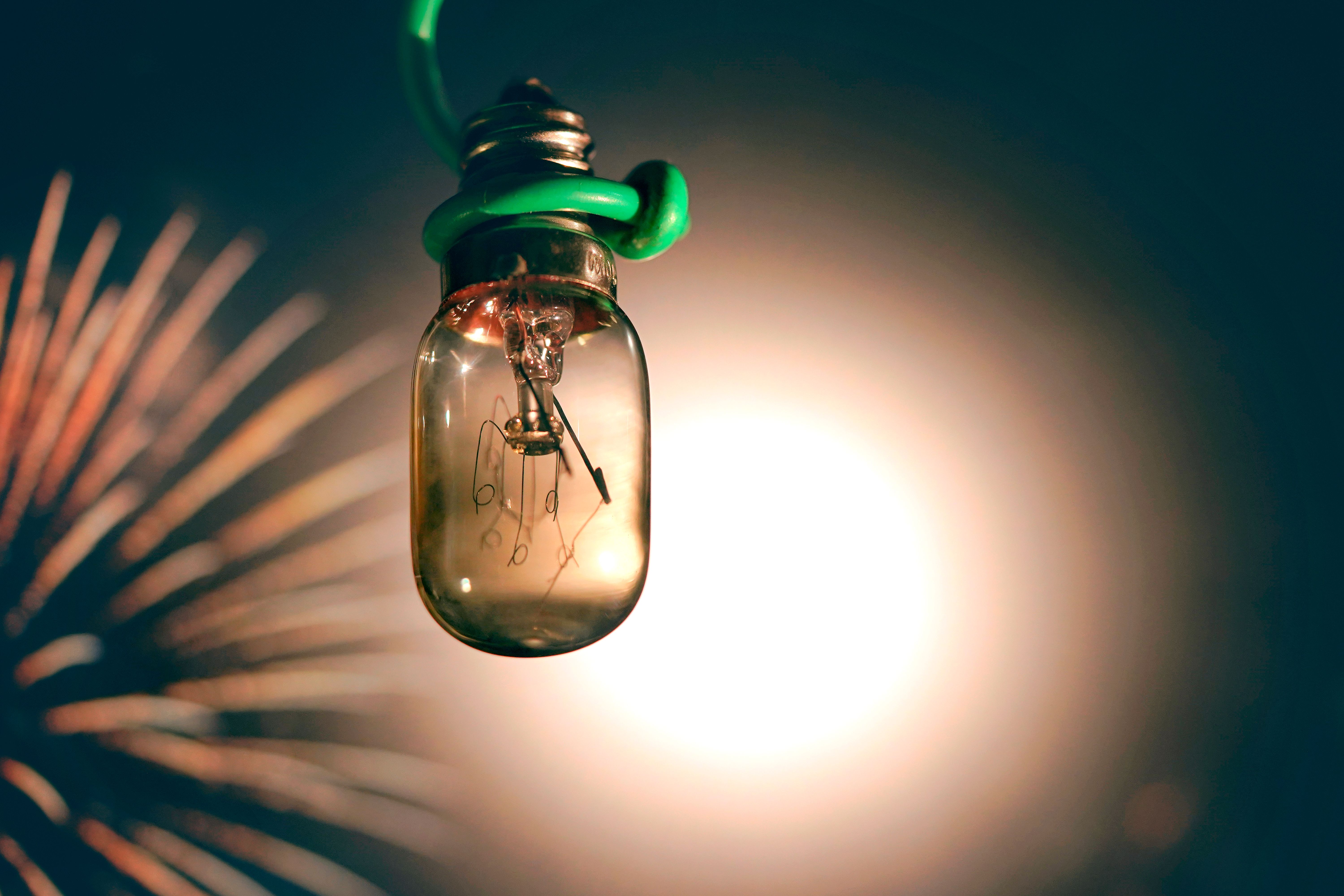 Vue rapprochée d'une ampoule lumineuse sur un arrière-plan flou avec des feux d'artifice, créant une ambiance vibrante et artistique.