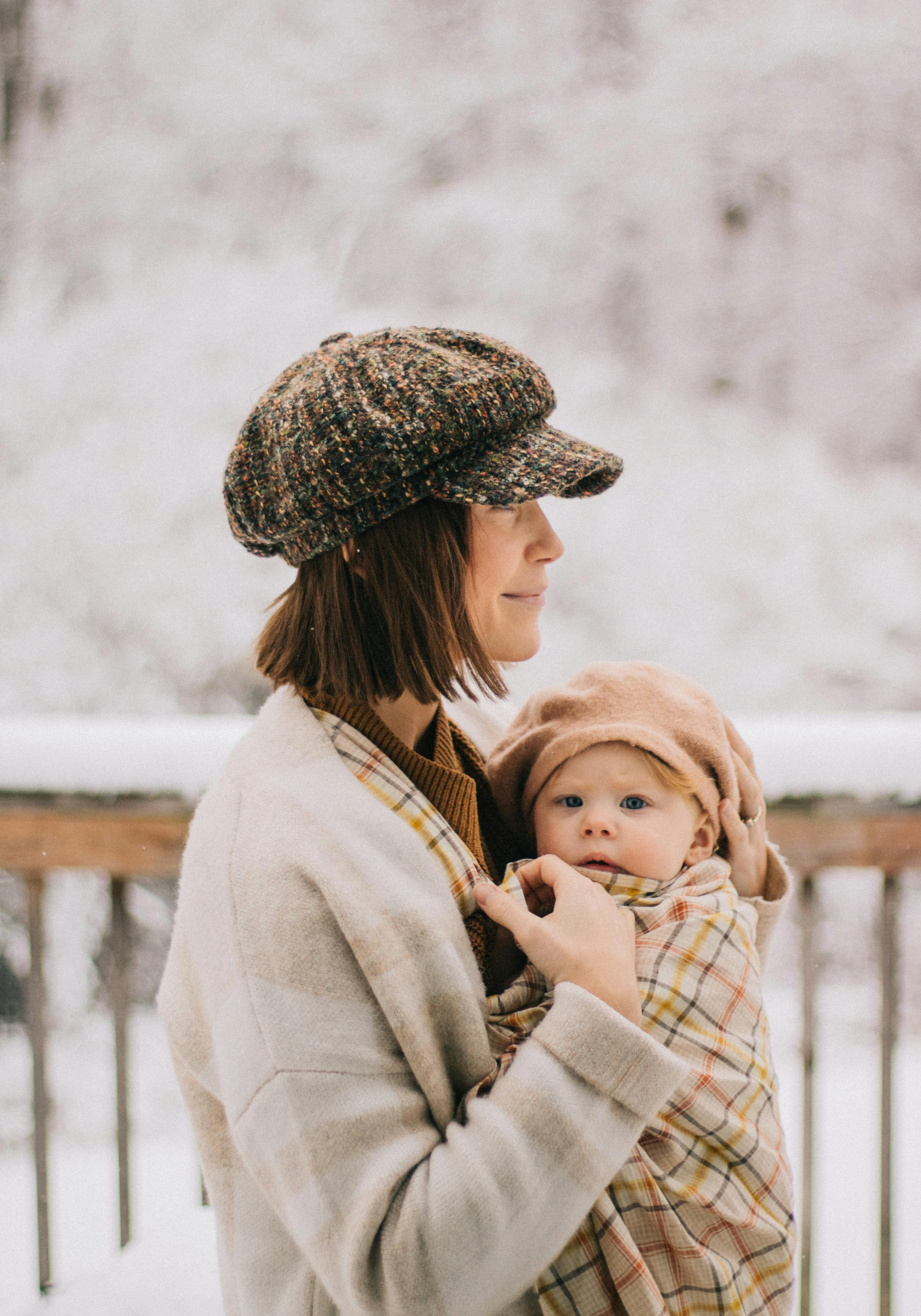 A stylish mother embraces her child in a serene snowy landscape.