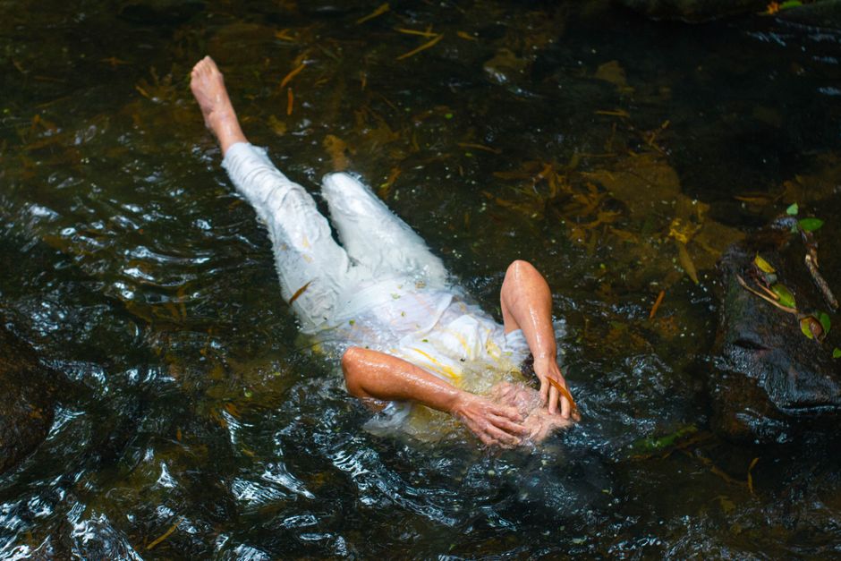 A person in white clothing lying down in a peaceful stream, surrounded by clear water.