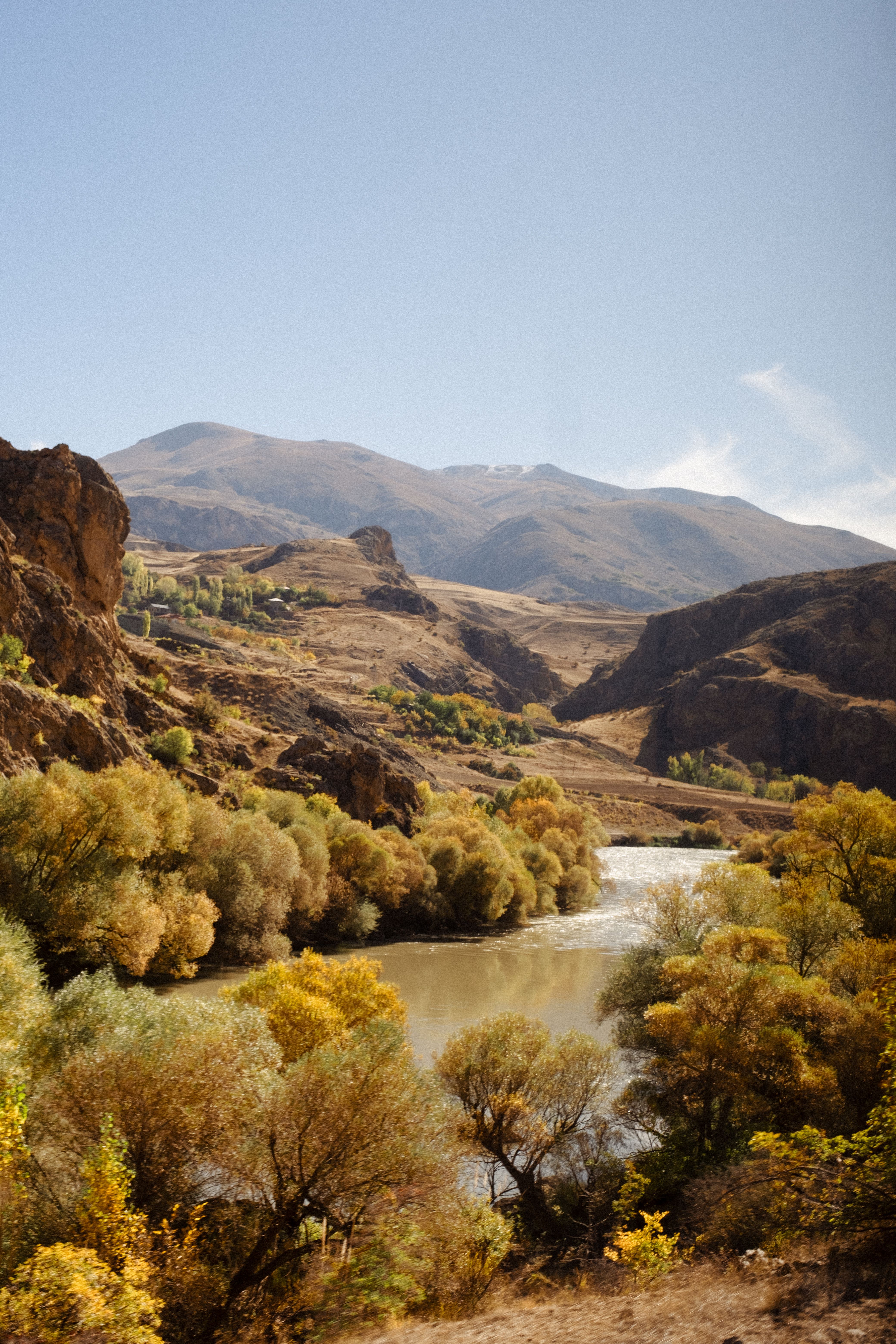 A picturesque autumn scene featuring a river surrounded by colorful foliage and towering mountains.