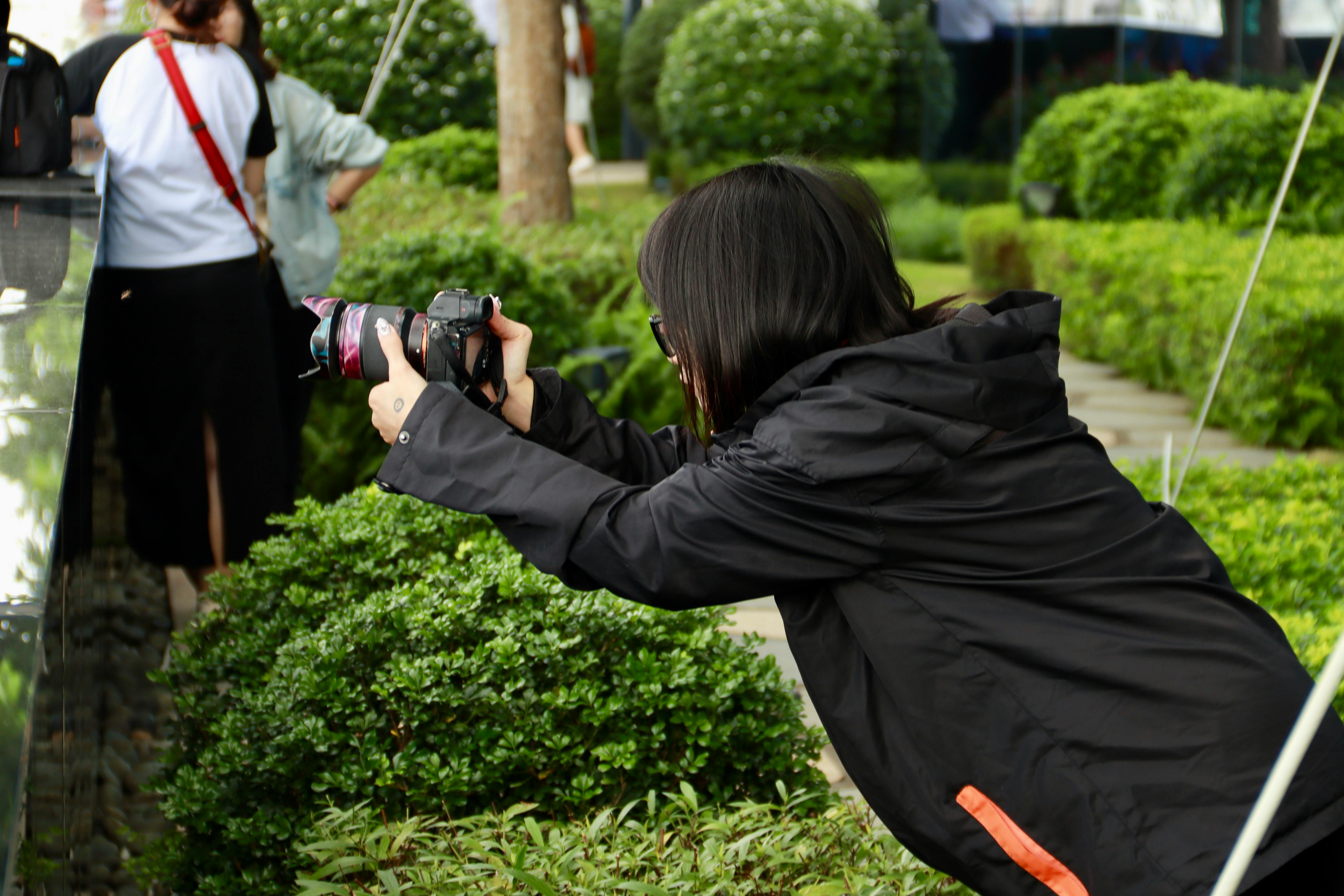 Woman photographing in a green garden, capturing plant details outdoors.