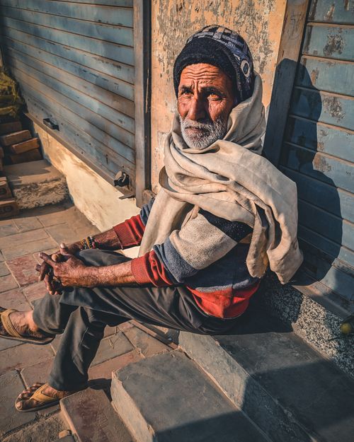Free Old man wearing traditional attire sitting in sunlight on a street in India. Atmospheric, warm lighting. Stock Photo