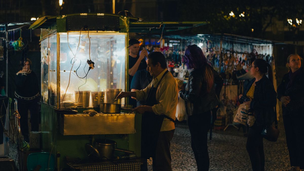 Bustling night market street scene featuring food vendor and customers at street stall.