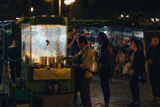Bustling night market street scene featuring food vendor and customers at street stall.