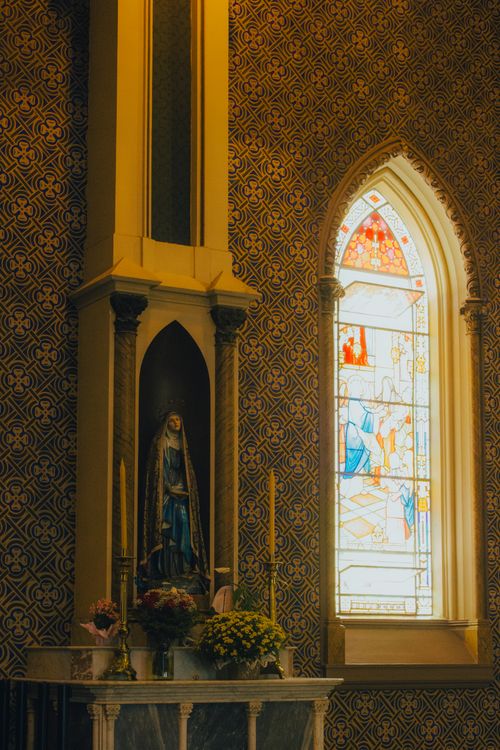Free Elegant church interior featuring a stained glass window with religious themes and a statue of Mary. Stock Photo