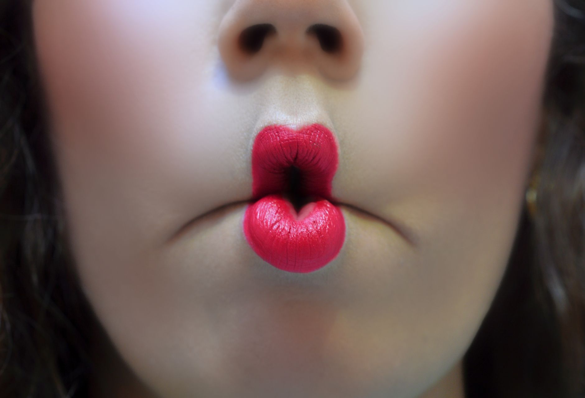 Artistic close-up of red-lipsticked lips making a playful fish face expression.