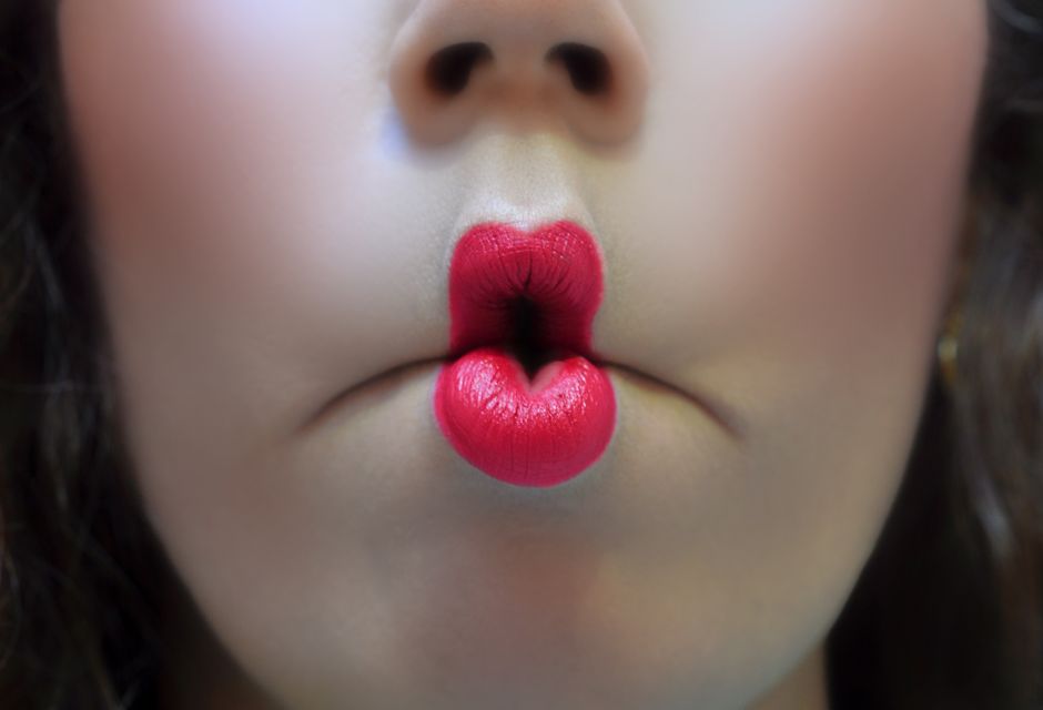 Artistic close-up of red-lipsticked lips making a playful fish face expression.