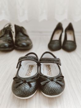 Close-up of shiny black children's shoes with bow design on a light wooden floor.