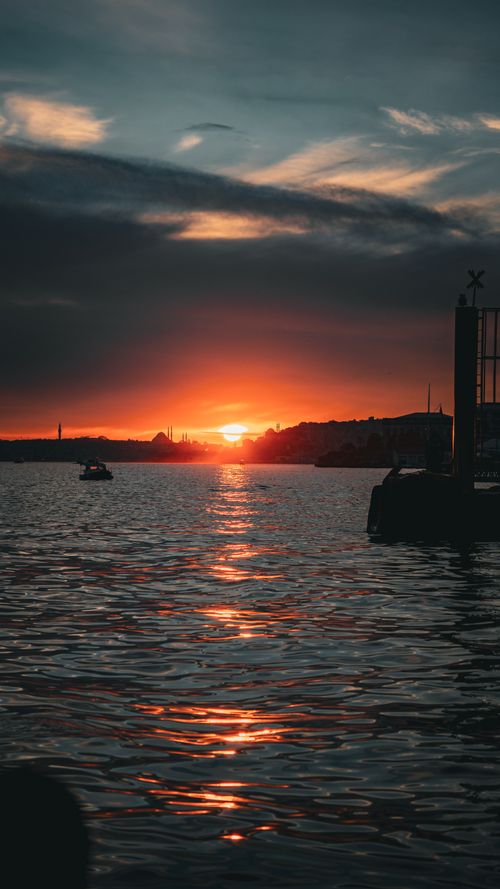 Free Breathtaking sunset over calm waters with silhouette of distant shoreline. Perfect peaceful evening scene. Stock Photo
