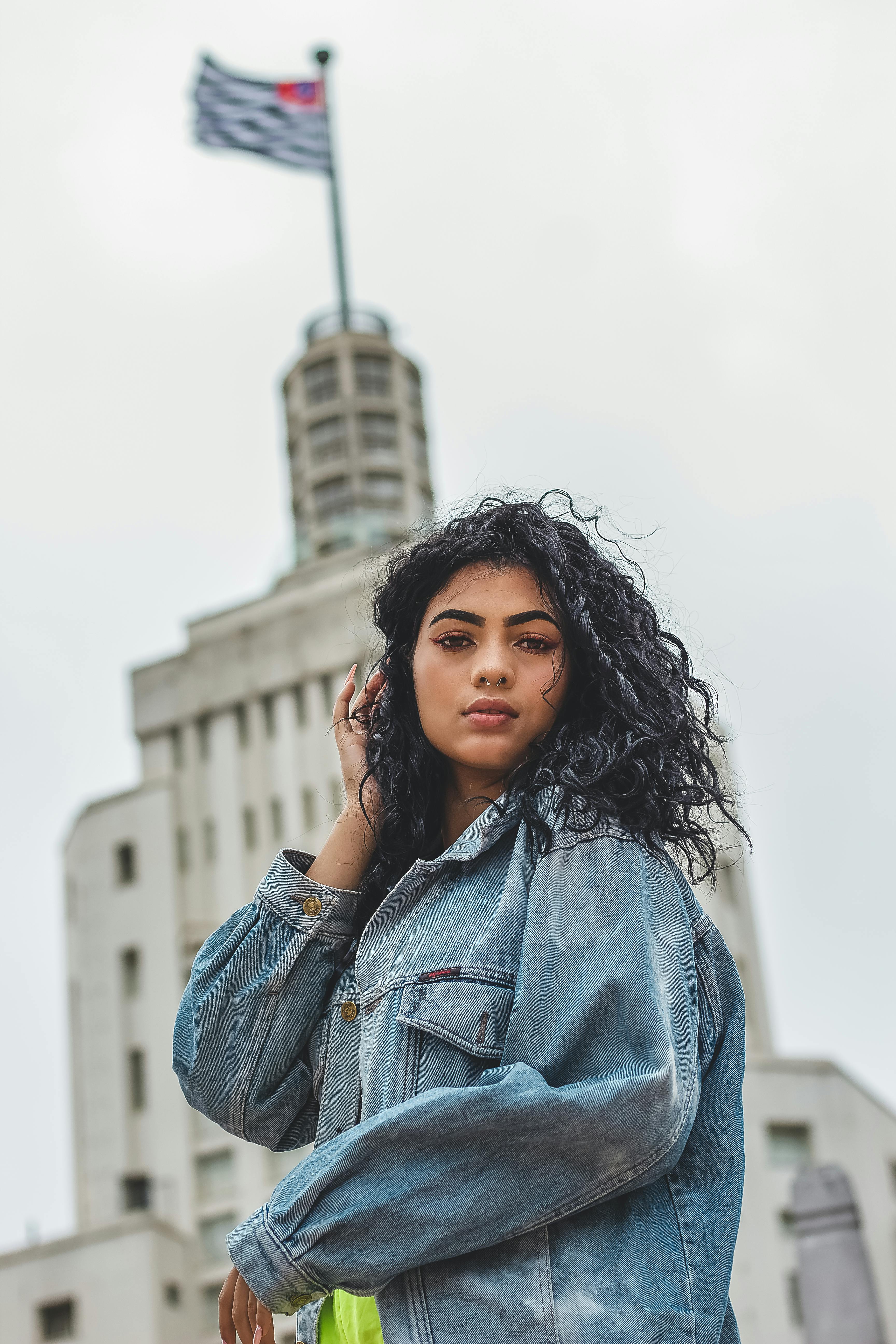 一名女子身穿牛仔夹克，在一座历史悠久的建筑前摆姿势