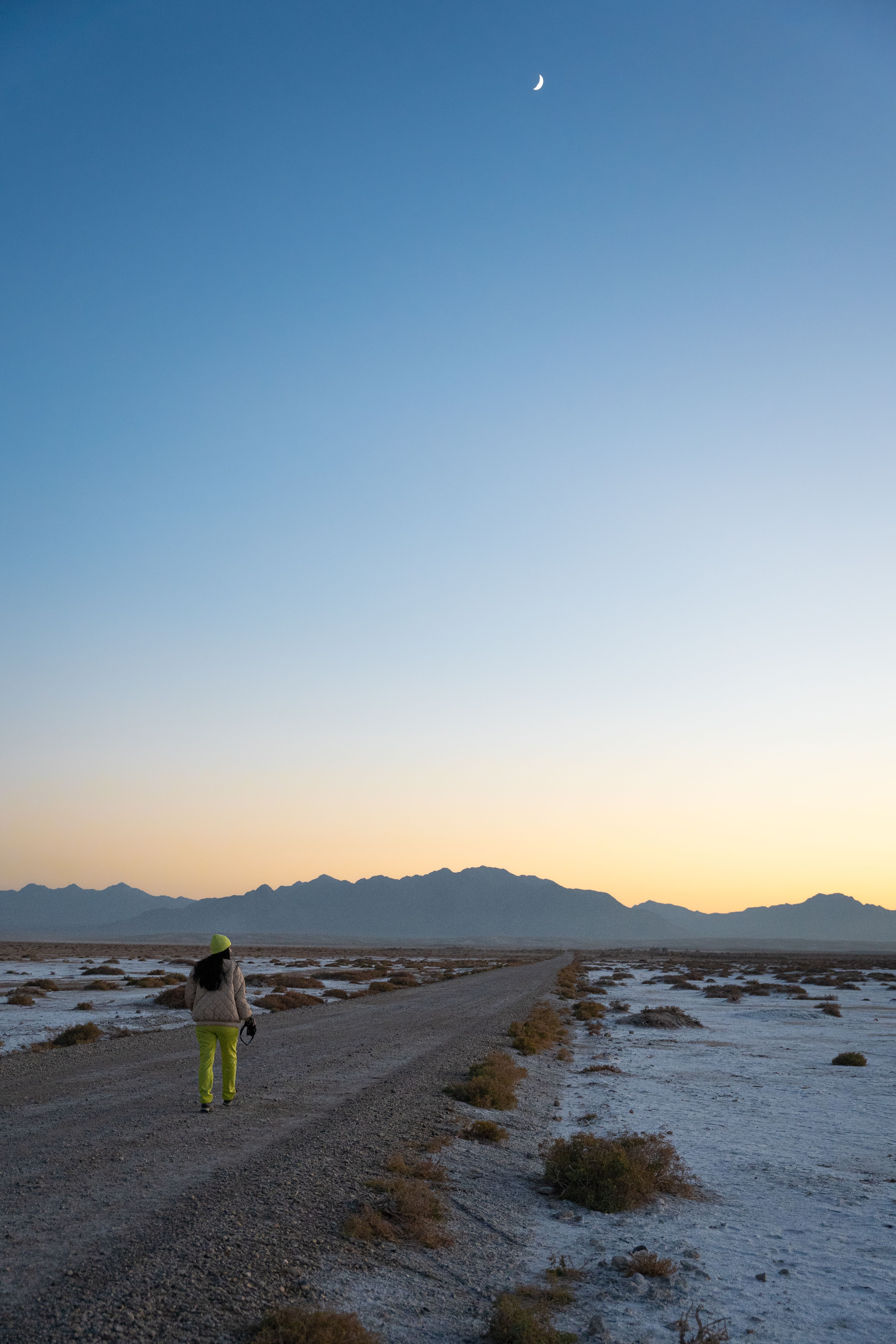 Person walking in Semnan desert under crescent moon light, serene evening.