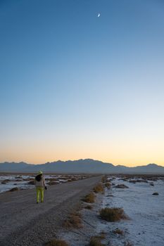 Person walking in Semnan desert under crescent moon light, serene evening.