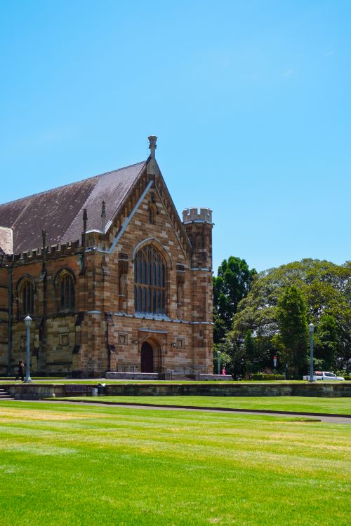 Free A beautiful Gothic-style building surrounded by vibrant grass under a clear blue sky. Stock Photo