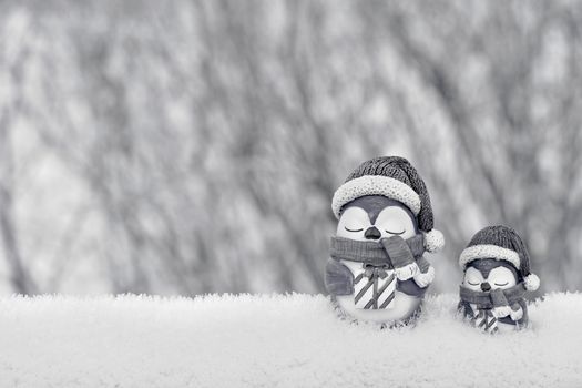 Cute penguin figurines in winter hats and scarves on a snowy background.