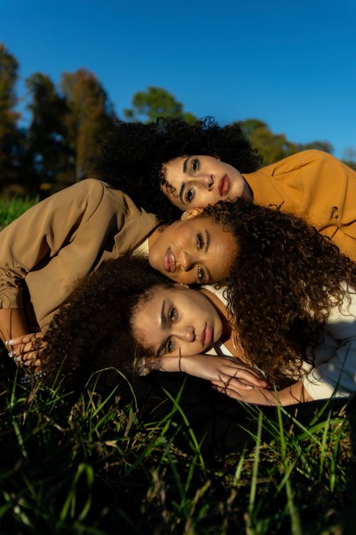 Free Three women with curly hair lying on grass enjoying a sunny day in Atlanta. Stock Photo