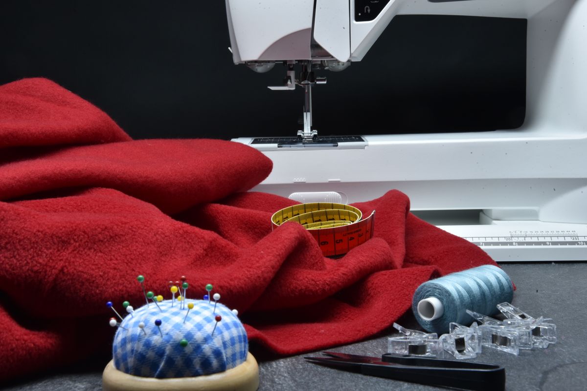 Close-up sewing setup with red fabric, a sewing machine, thread, and measuring tape