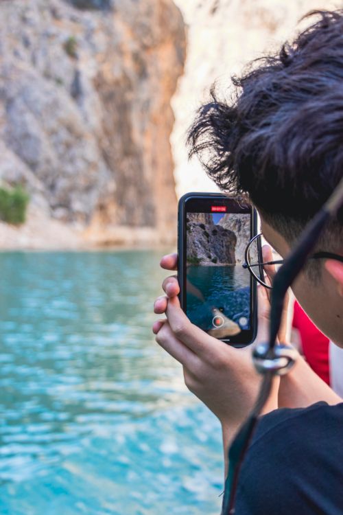 Free Person takes photo with smartphone near blue water and rocky cliff outdoors. Stock Photo