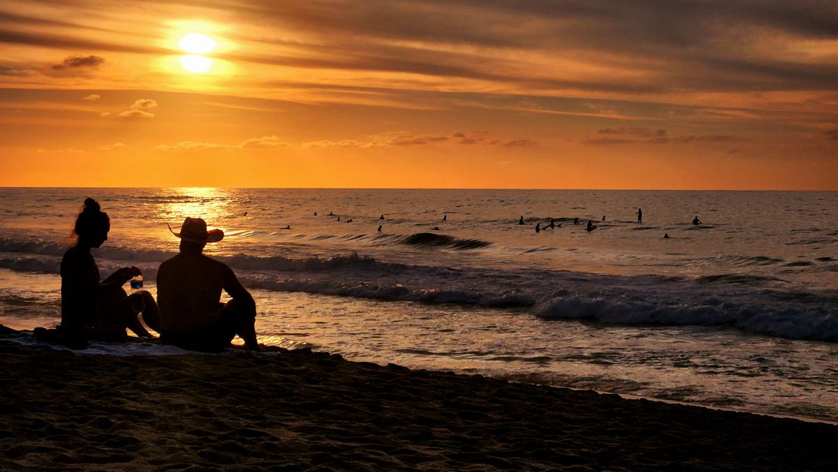 Silhouette of a couple enjoying a sunset on San Pancho beach. Surfers in the ocean.