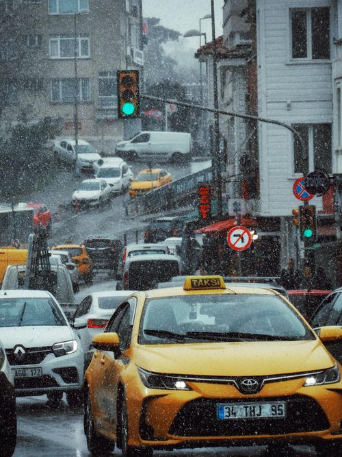 Free A rainy day on an urban street filled with traffic, featuring a prominent yellow taxi and multiple vehicles. Stock Photo