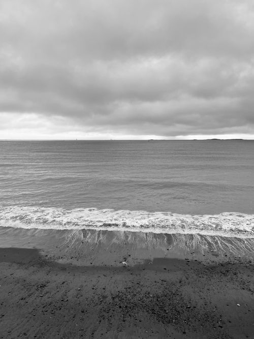 Free A tranquil black and white photograph of a beach with gentle waves and an overcast sky. Stock Photo