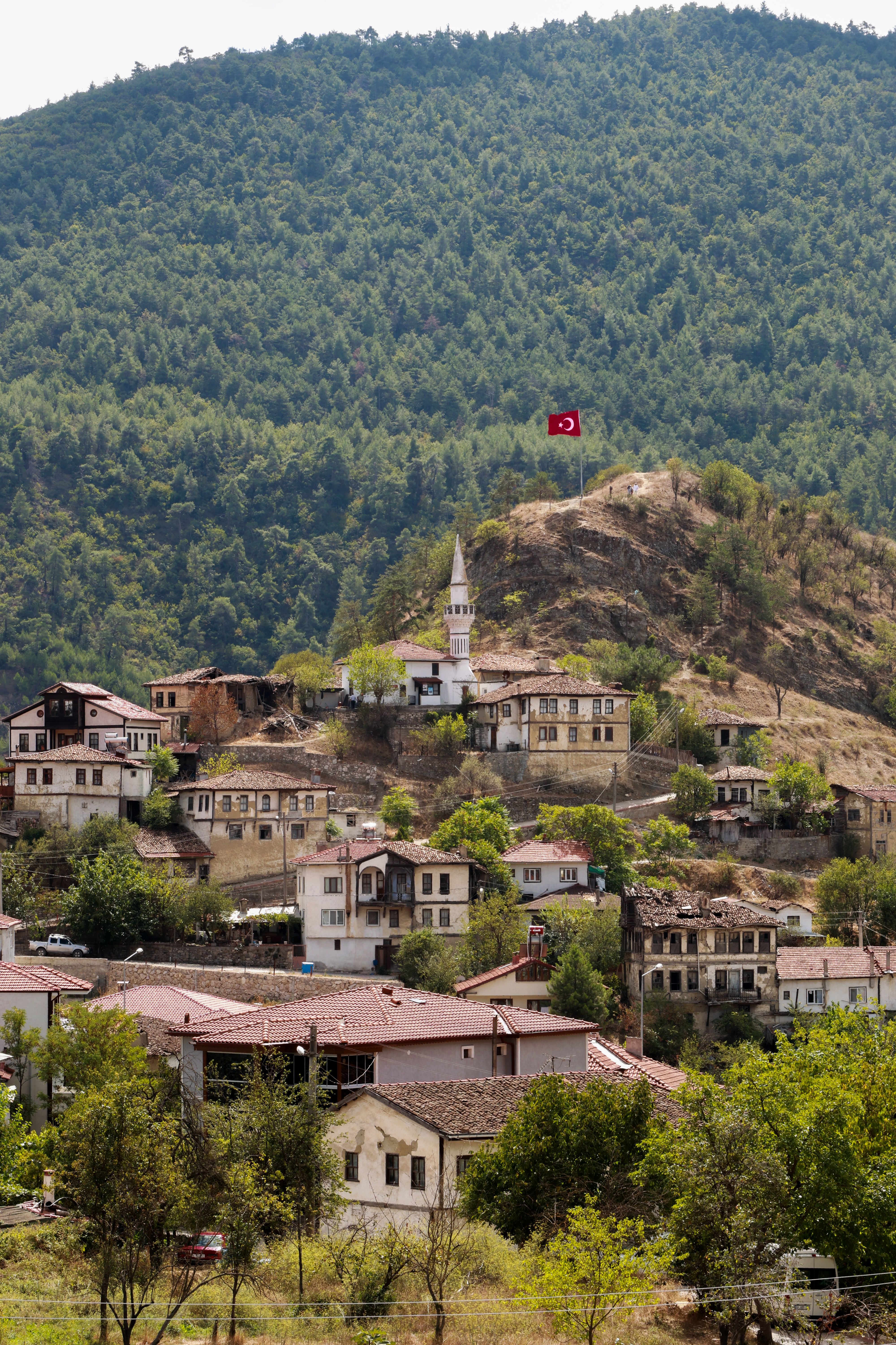 A picturesque view of a traditional Turkish village nestled in lush green hills with a prominent Turkish flag.