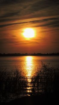 Beautiful sunset over lake in San Miguel del Monte, Argentina, with warm orange sky and reflecting water.