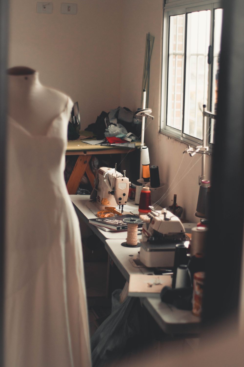 Witte jurk op een paspop naast een naaimachine in het atelier