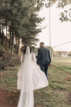 A couple walks outdoors in wedding attire, surrounded by trees. Perfect bridal moment.
